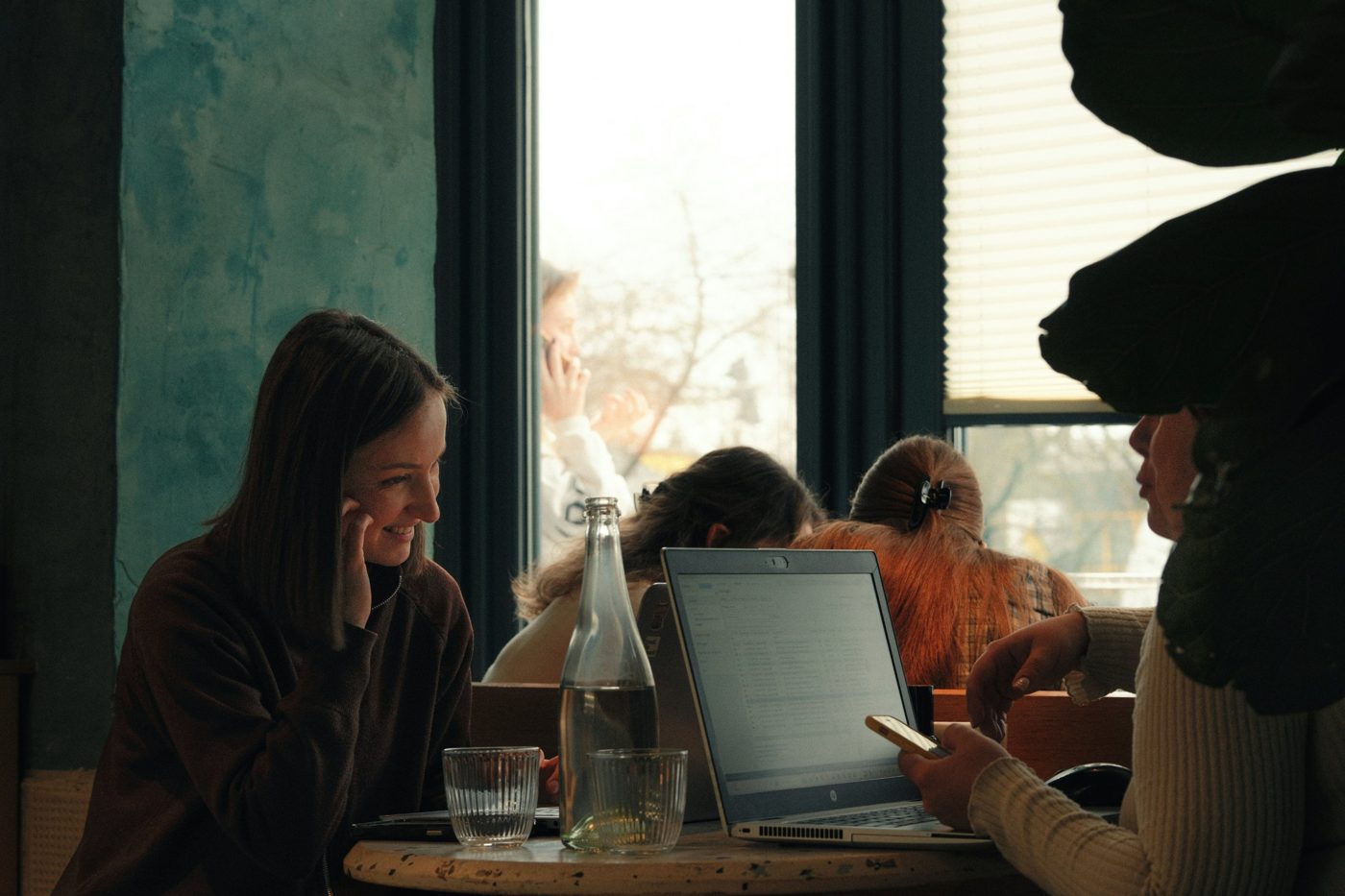 Women working on laptops together at a café table by the window